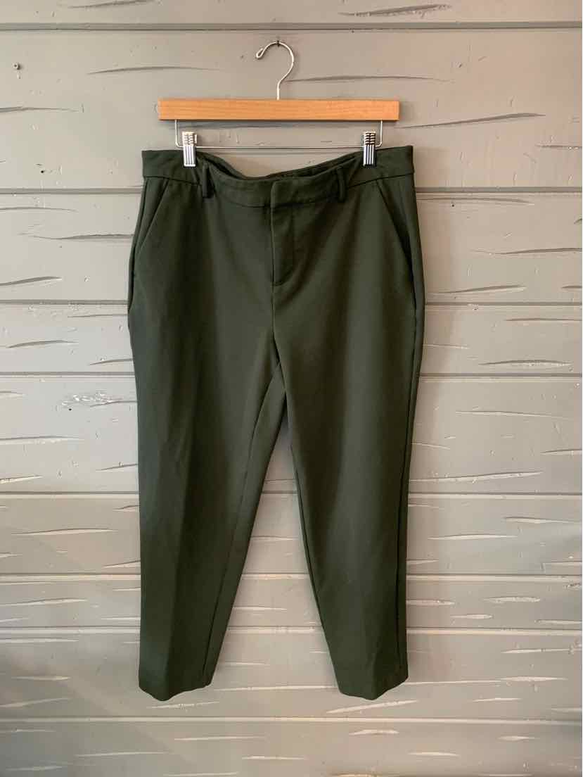 Olive green tapered pants with a high waist and belt detail hanging against a wooden wall.