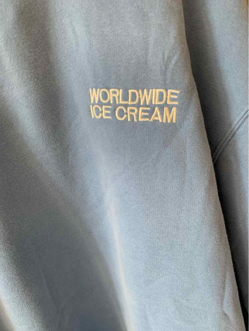 Black sweatshirt sleeve with small yellow "WORLDWIDE ICE CREAM" text embroidered on it.