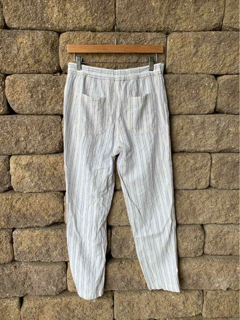 White ankle-length pants with vertical thin black stripes and elastic waistband hanging on wooden hanger.