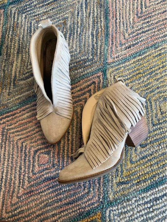 Beige suede ankle boots with fringe detailing and block heels on patterned rug.