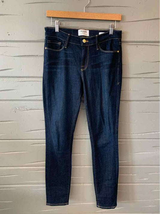 Dark blue slim-fit denim jeans with classic five-pocket design hanging on wooden hanger against gray wooden wall.