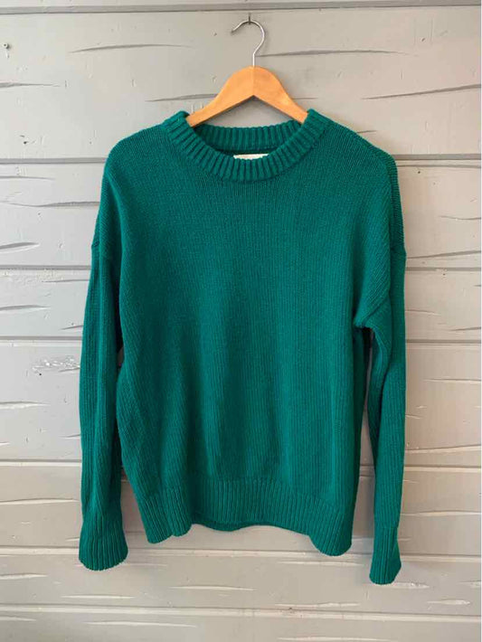 Teal green knit sweater with ribbed crew neckline, cuffs, and hem, shown on wooden hanger against white wall.