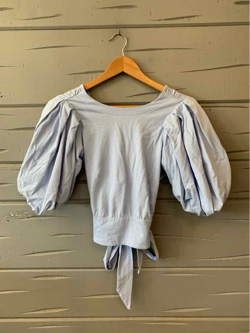 Light blue blouse with puffed three-quarter sleeves and tie waist detail hanging on wooden hanger.