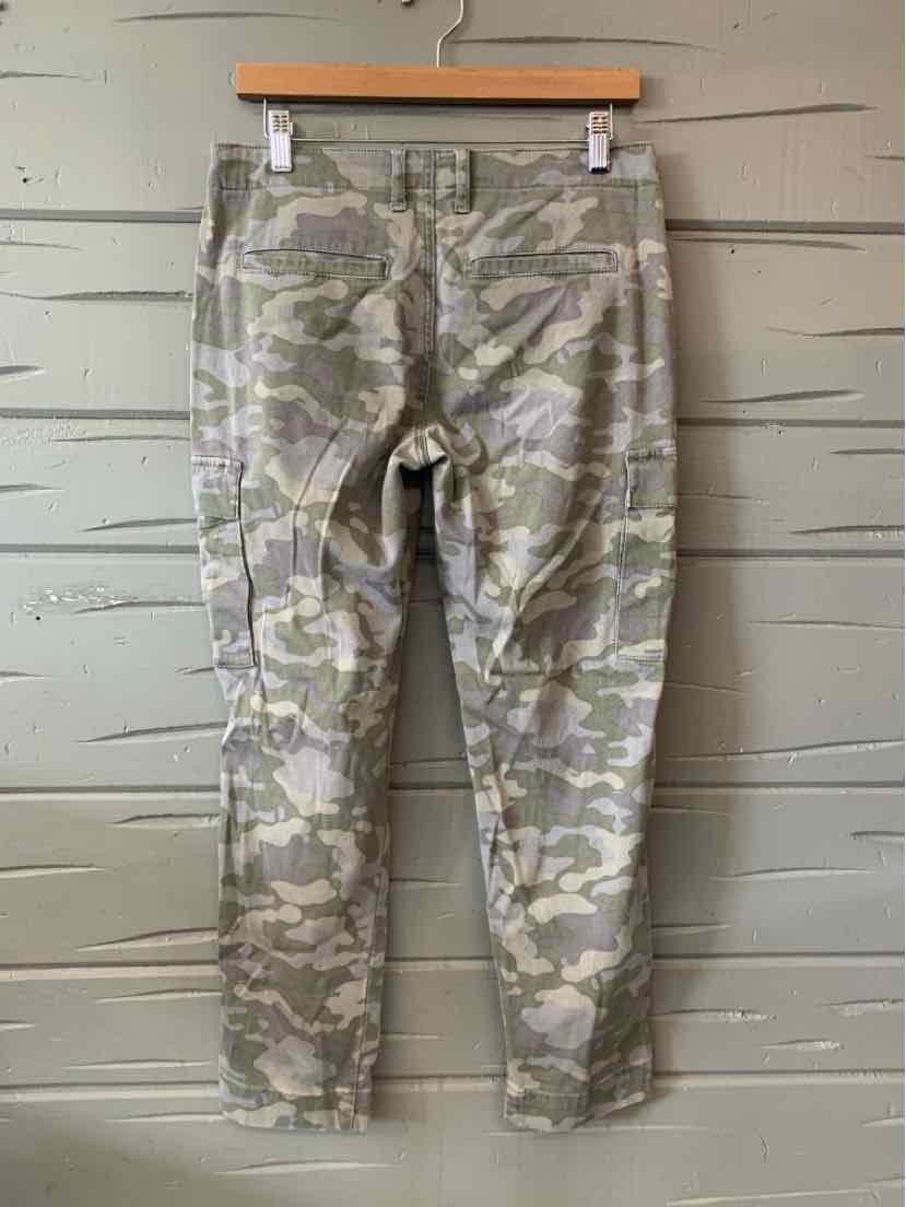 Slim-fit camouflage pants in shades of green and beige with back pockets and belt loops, hanging on wooden hanger.