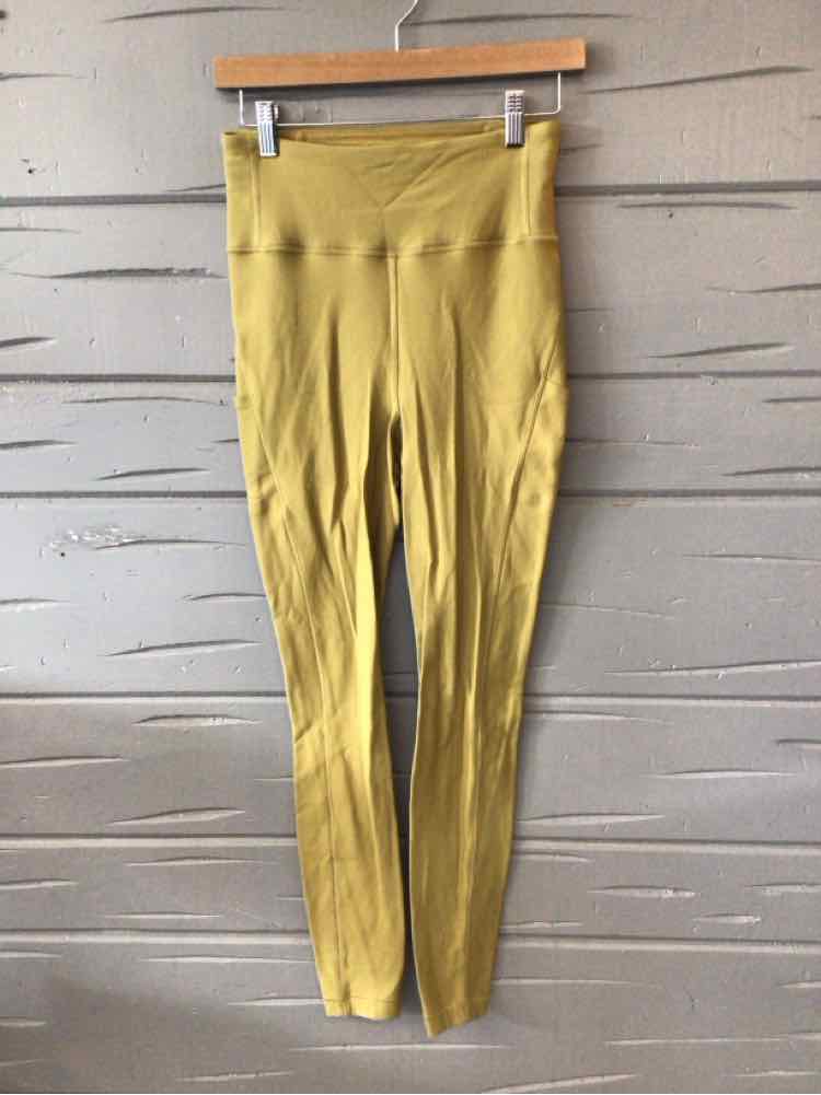 High-waisted solid green Lululemon leggings with smooth waistband and seamless design hanging on wooden hanger against gray.