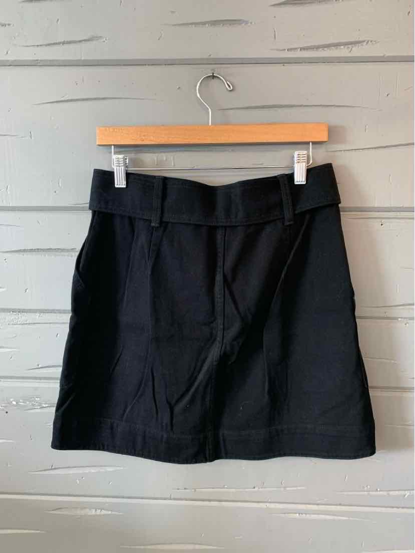 Black knee-length skirt with tailored fit, belt loops, and front seam details hanging on wooden hanger.
