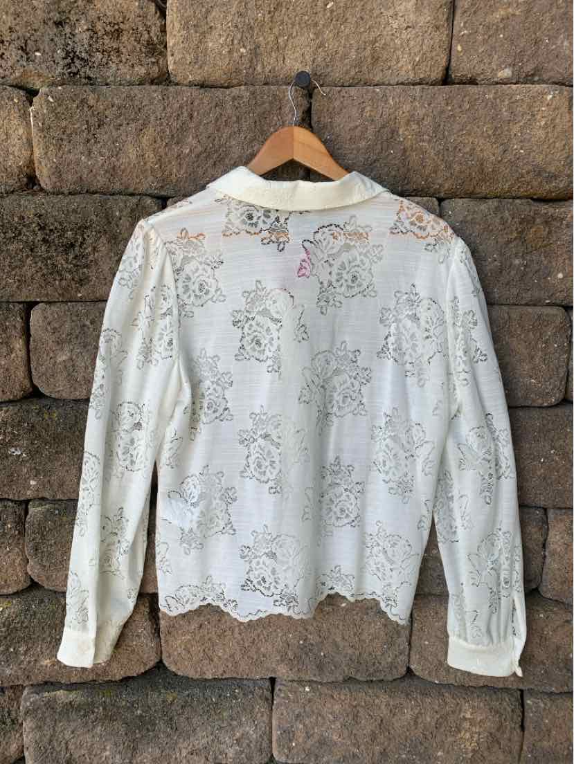 White long-sleeve lace blouse with floral patterns and scalloped hem on wooden hanger.