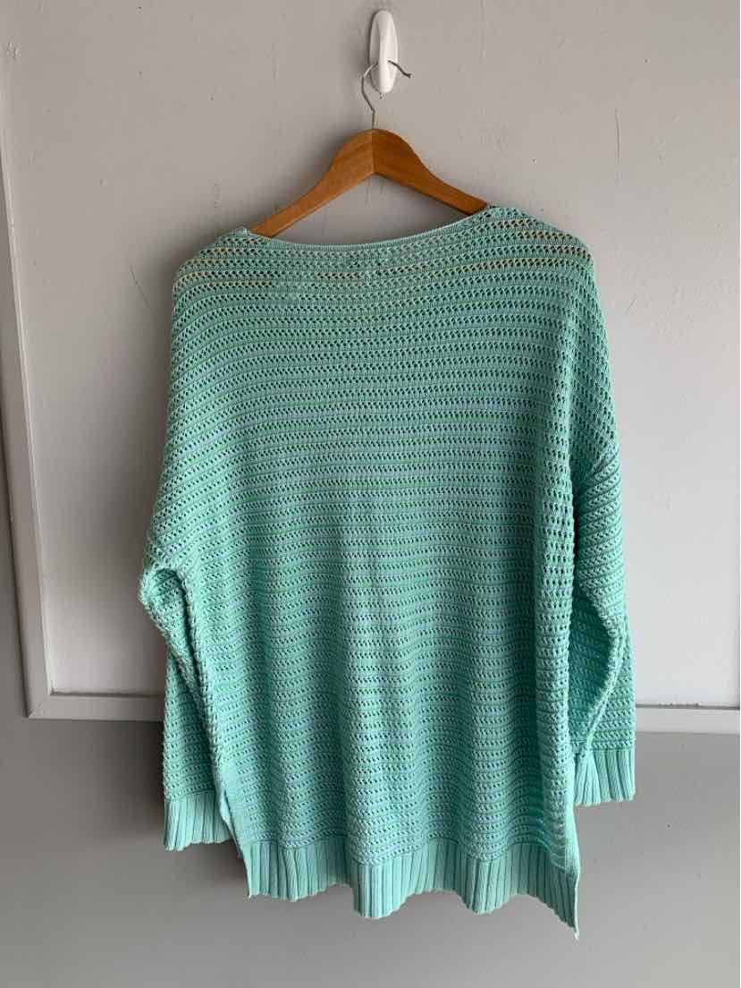Light blue knit sweater with ribbed cuffs and hem hanging on wooden hanger against white wall.