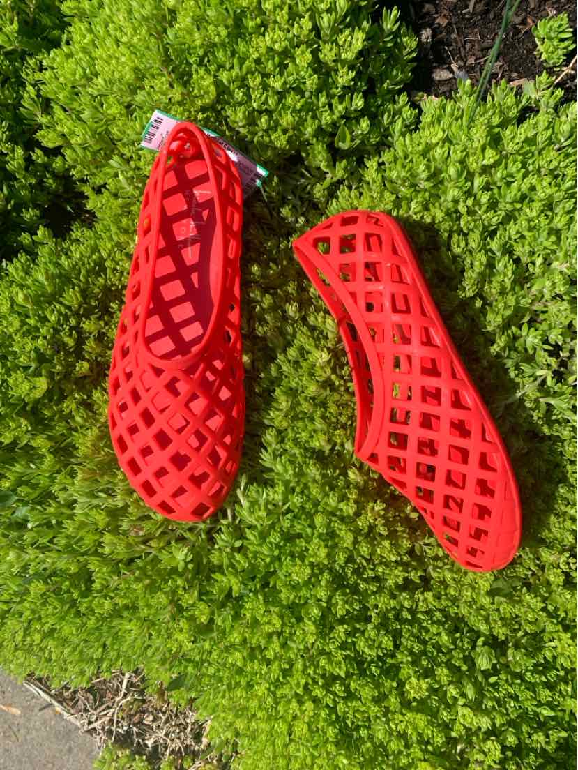 Red lattice-patterned flat shoes with round toes, size 7, placed on green foliage background.