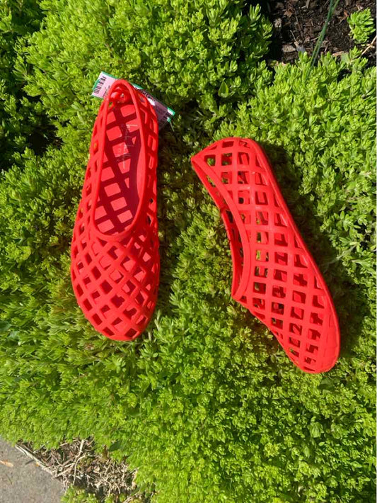 Red lattice-patterned flat shoes with round toes, size 7, placed on green foliage background.