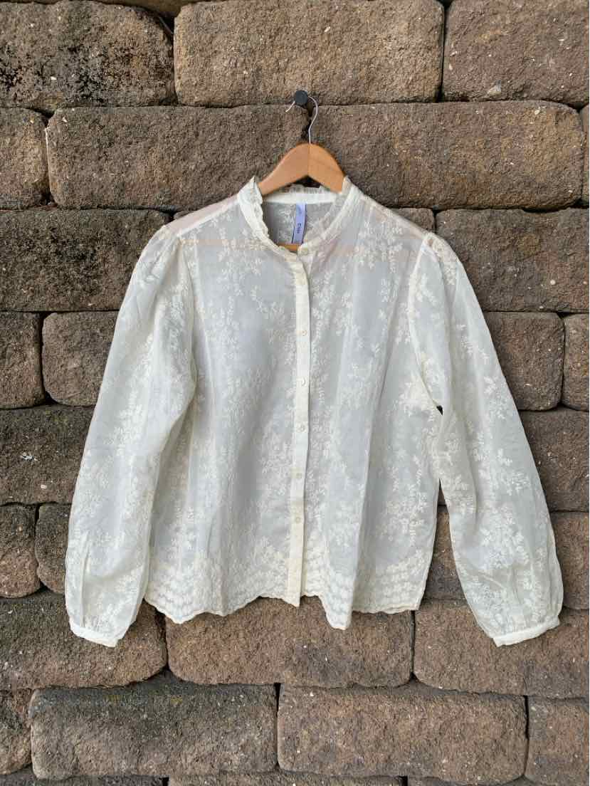 White long-sleeve floral lace blouse with button-up front and gathered cuffs on wooden hanger.