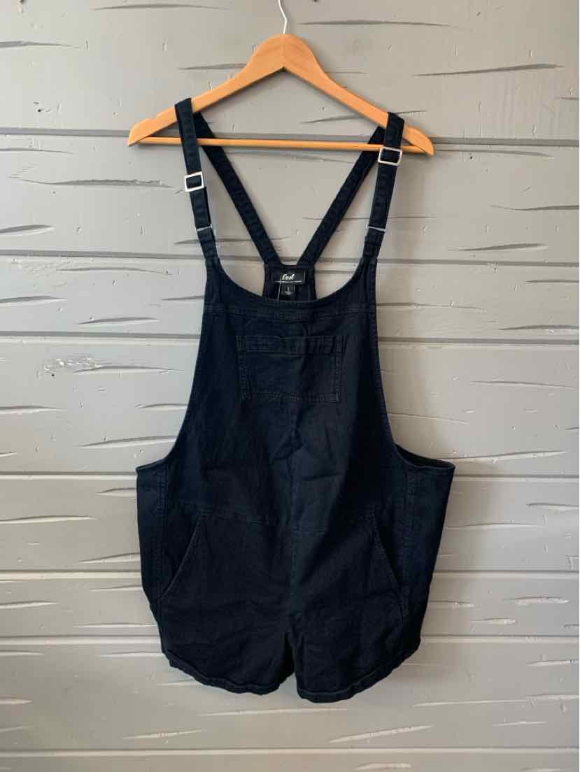 Black sleeveless denim overalls with adjustable shoulder straps and two front pockets hanging on wooden hanger.