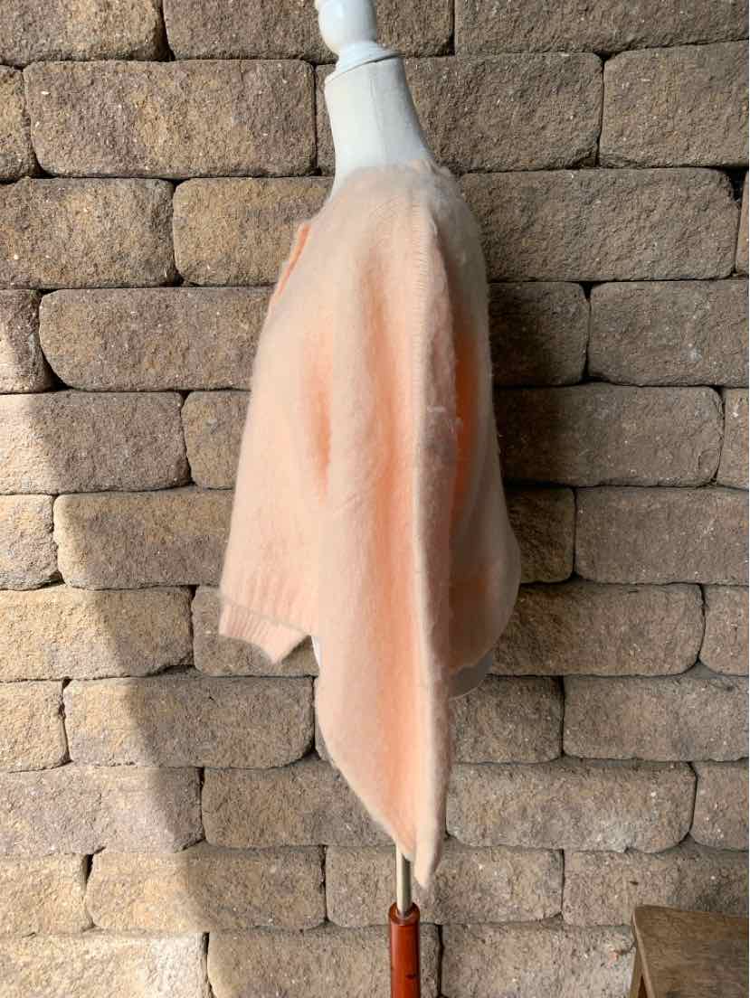 Soft peach solid-fabric garment on a wooden hanger, shown against a stone wall.