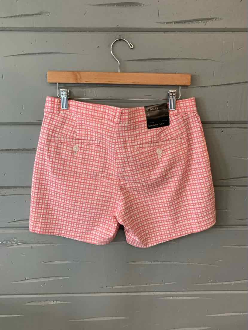 Pink and white checkered high-waist shorts with back pockets and belt loops hanging on wooden hanger.