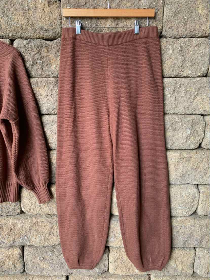 Brown knit pants with elastic waistband and cuffs, hanging against a stone wall.