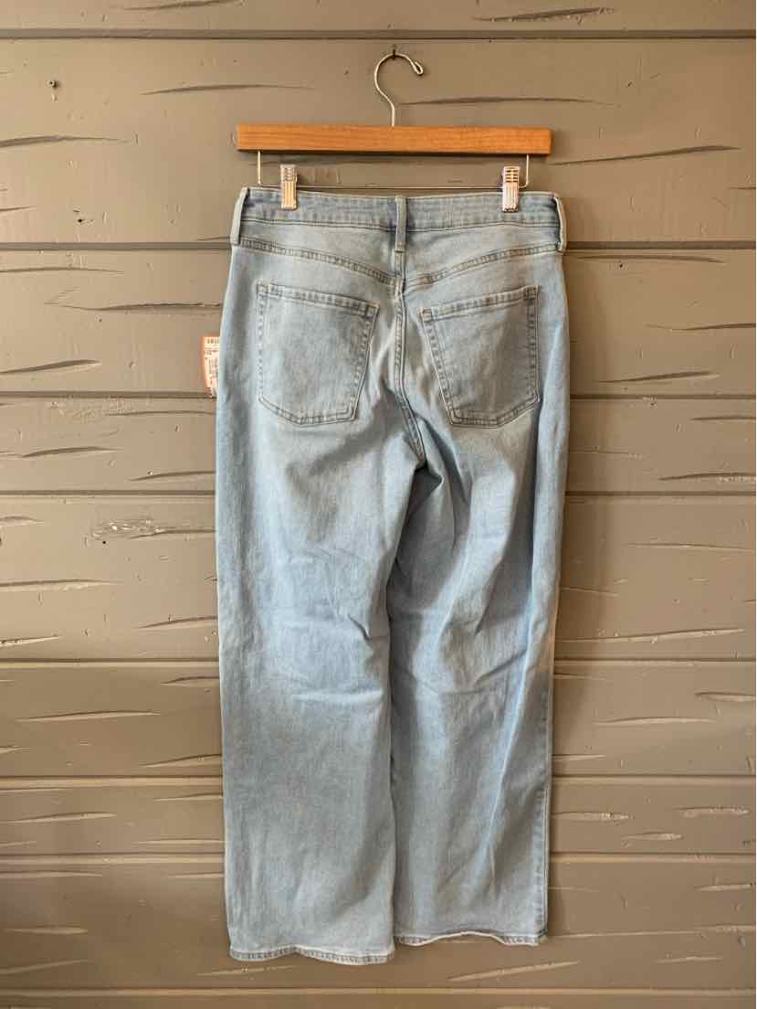 Light blue denim jeans with a relaxed fit, straight legs, and back patch pockets hanging on a wooden hanger.
