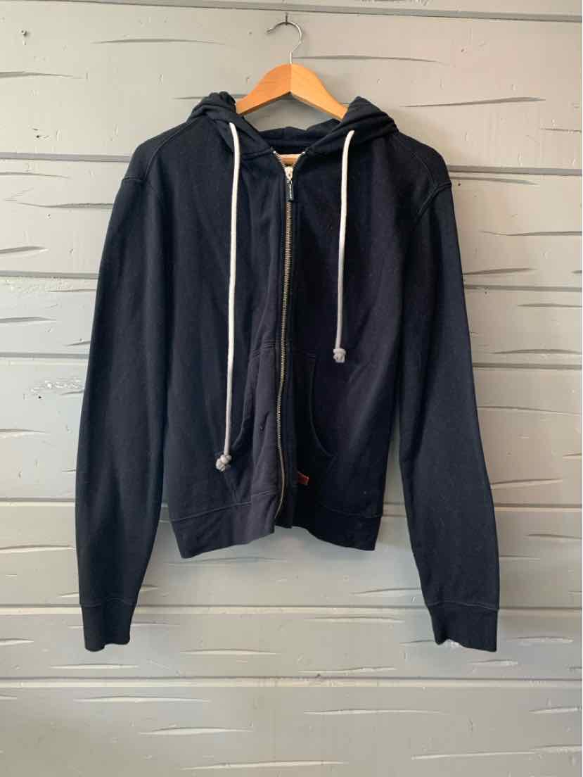 Black zip-up hoodie with a front zipper, drawstring hood, and long sleeves, hanging on a wooden hanger.
