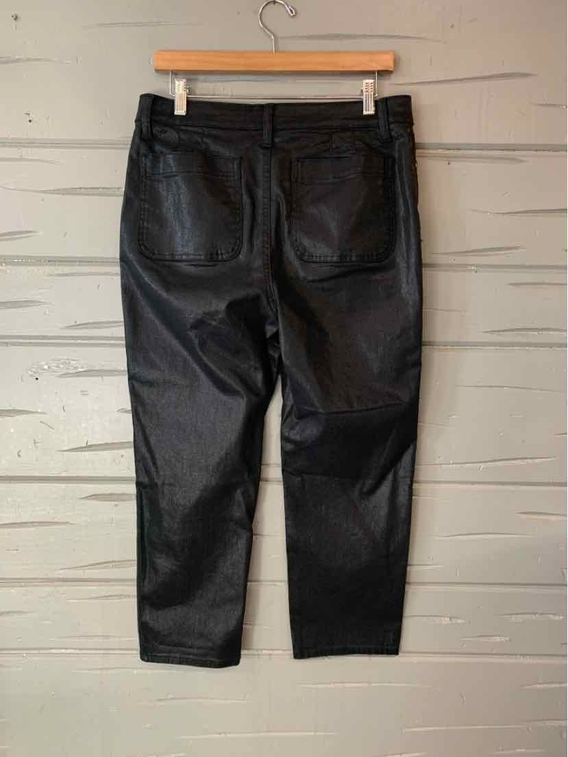 Black leather pants in size 10P with back pockets hanging on a wooden hanger against a white wooden wall.