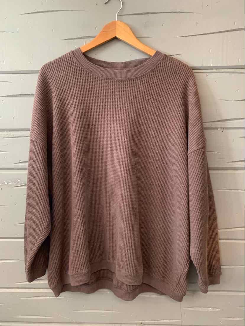 Mauve oversized knit sweater with long sleeves and crew neckline hanging on wooden hanger against white wooden wall.