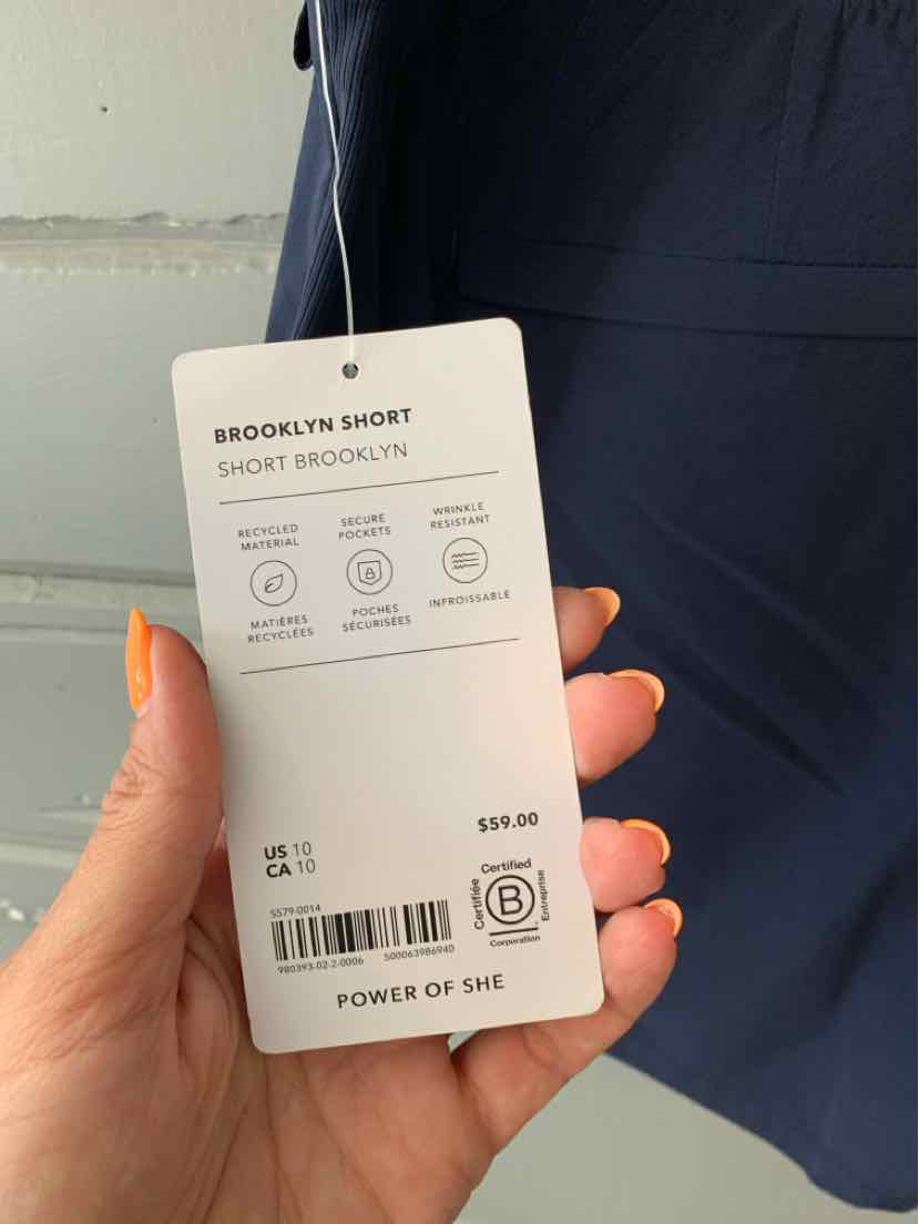 White rectangular clothing tag showing product details hanging from dark navy blue fabric shorts.