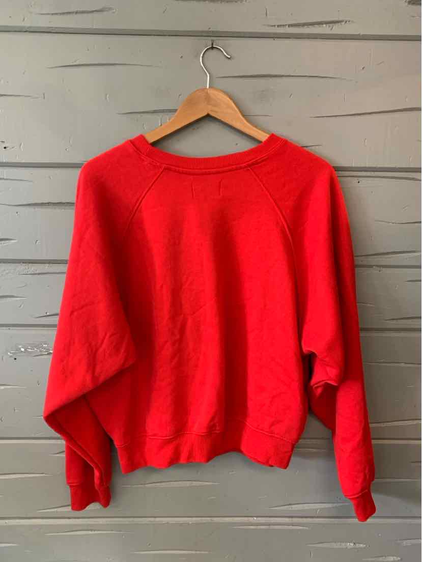 Red crewneck sweatshirt with long raglan sleeves and ribbed cuffs and hem, hanging on wooden hanger.