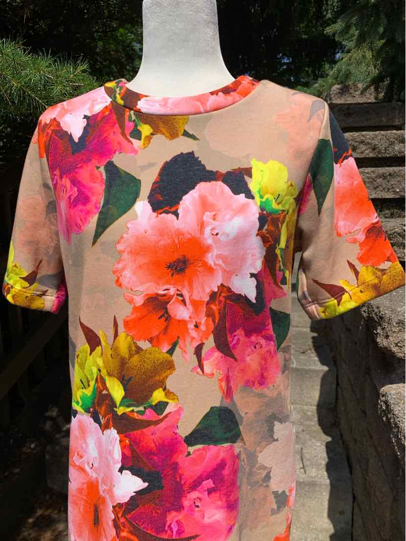 Short-sleeve crewneck top with vibrant multi-colored floral print on soft beige background.
