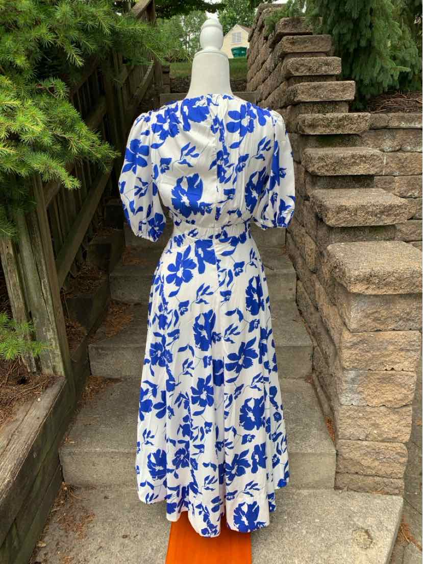 White midi dress with blue floral print, puff sleeves, fitted waist, and flowy skirt.