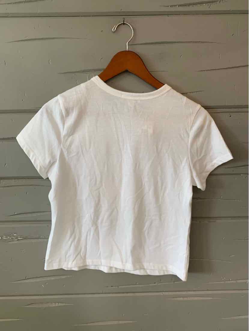 White short-sleeve cropped T-shirt with crew neckline on wooden hanger against gray paneled wall.