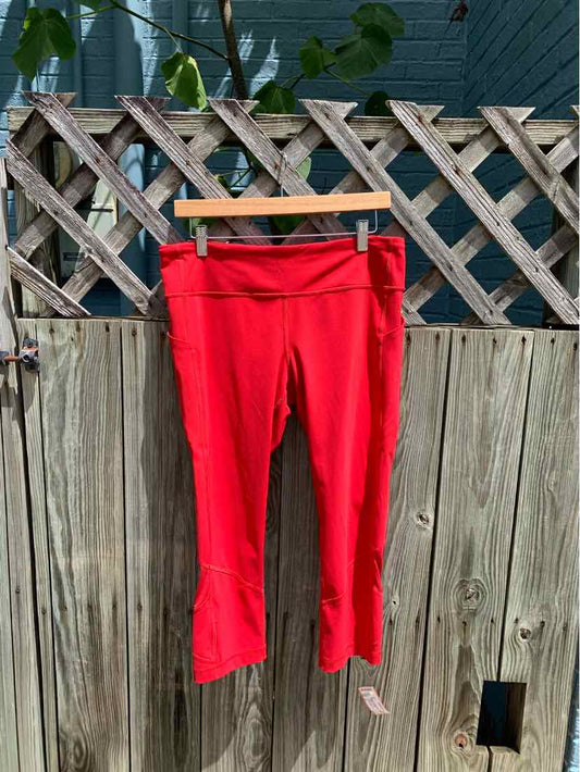 Bright red athletic capri leggings with fitted waistband, hanging on wooden hanger outdoors.