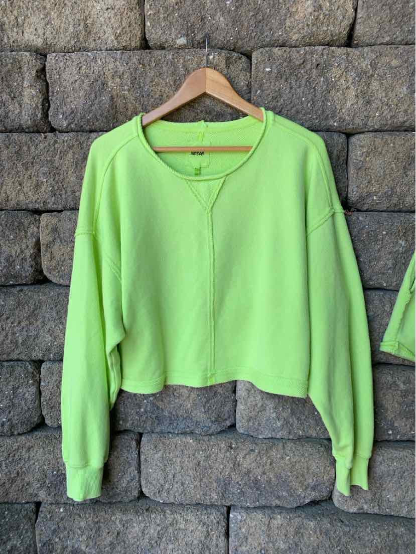 Light green long-sleeve cropped sweatshirt with V-neck and ribbed cuffs hanging on wooden hanger.