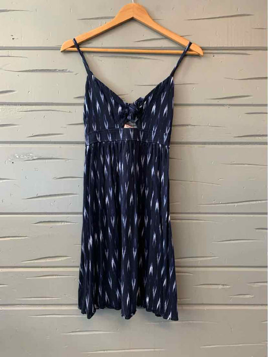 Navy blue sleeveless dress with white ikat pattern and front tie detail on wooden hanger.