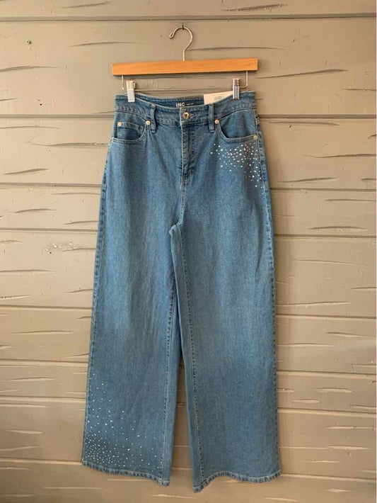 High-waisted blue denim jeans with wide legs and button closure on wooden hanger.
