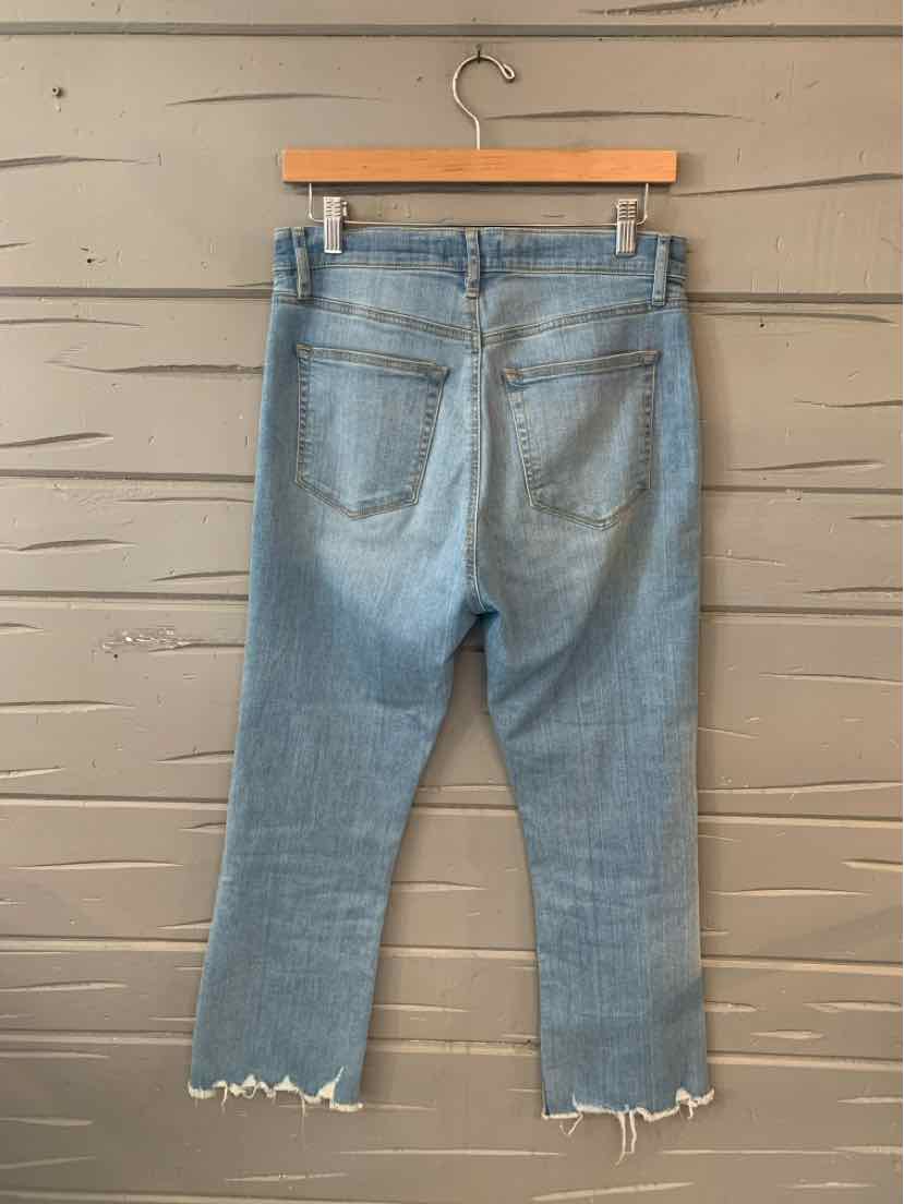 Light wash denim jeans size 8T with frayed hem and back pockets hanging on wooden hanger.