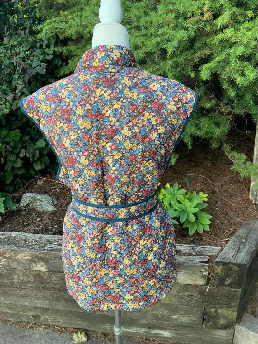 Floral patterned sleeveless vest with multicolored small flowers and a cinched waist belt.