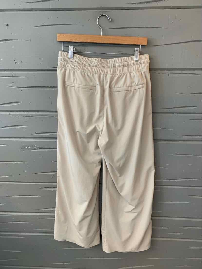 Beige wide-leg pants with elastic waistband and two back patch pockets hanging on wooden hanger.