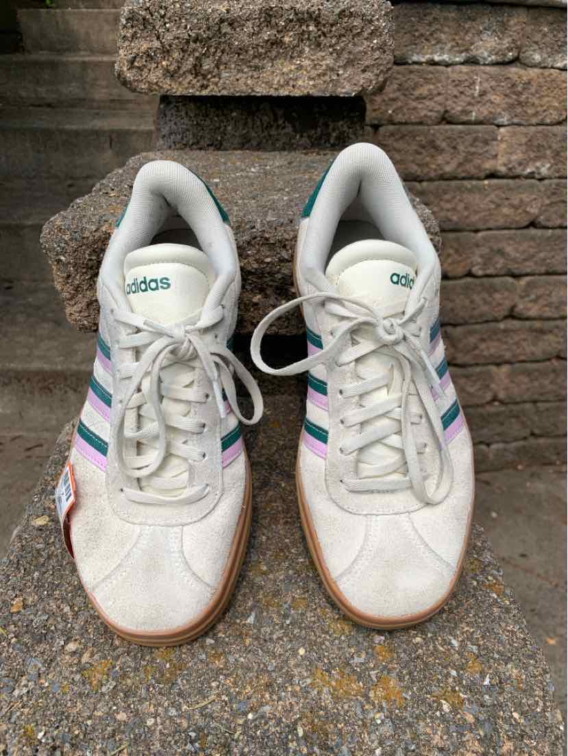 White low-top Adidas sneakers with gray suede overlays, pink and blue stripes, and gum rubber soles, size 7.5.