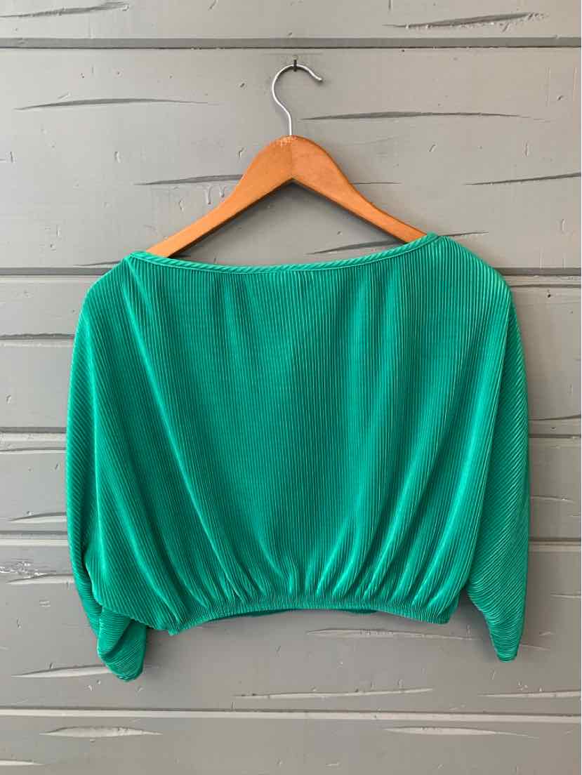 Green long-sleeve cropped top with gathered elastic hem on wooden hanger against gray wooden wall.