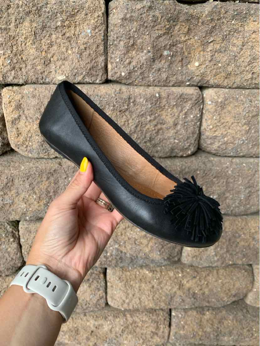 Black leather ballet flat with rounded toe and large pom-pom detail on front.