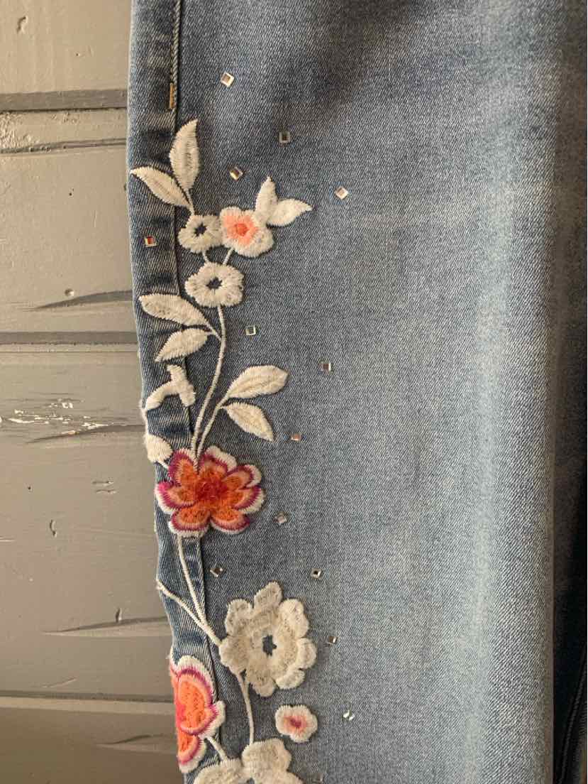 Light blue denim jeans with embroidered floral design in orange, white, and green along the leg.