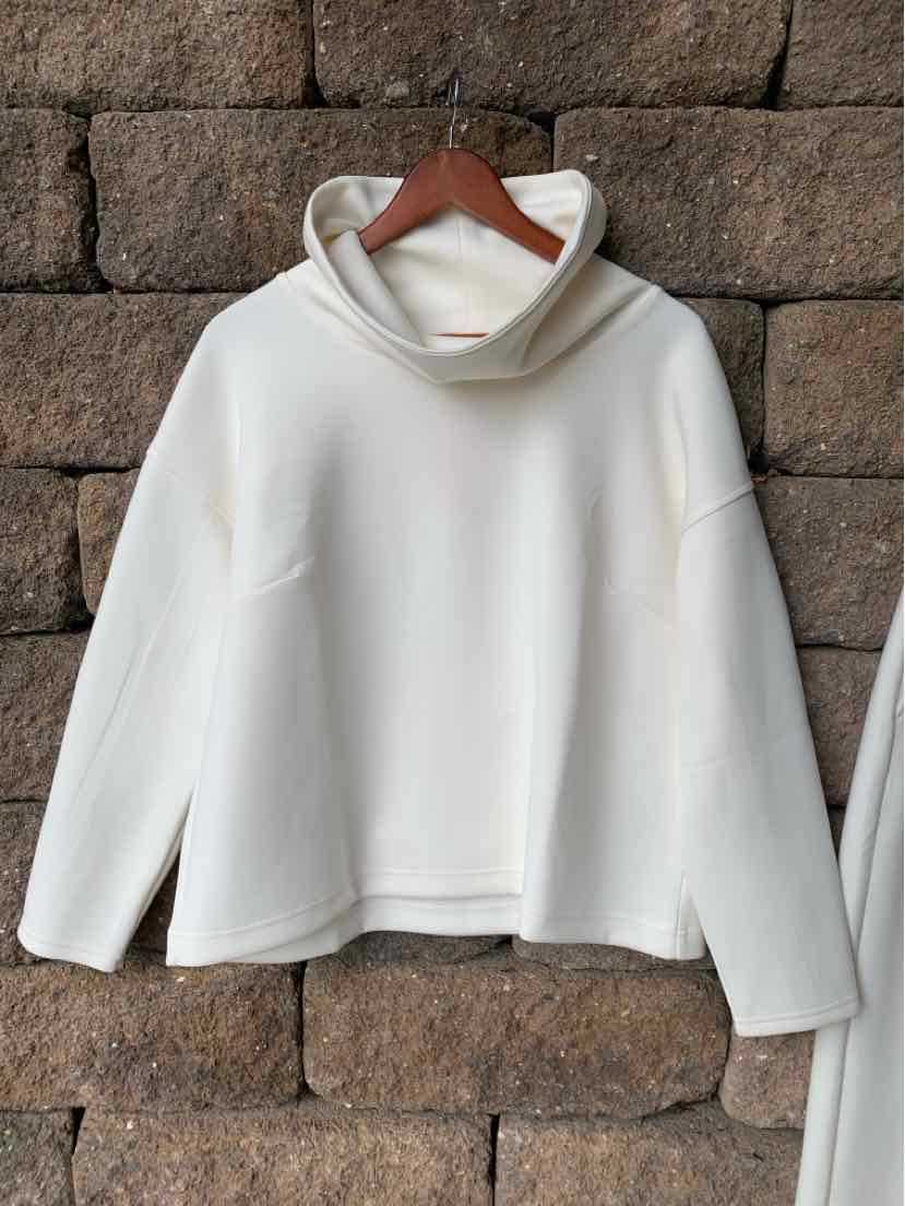 Cream-colored long-sleeve pullover with a loose cowl neck and relaxed fit hanging on wooden hanger.