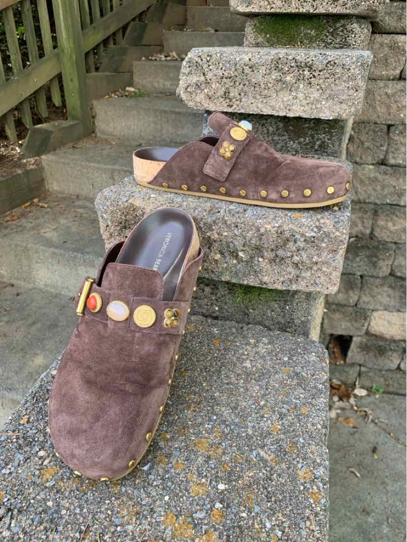 Brown suede Veronica Beard clogs with open backs, wooden soles, brass-tone studs, and decorative round medallions.