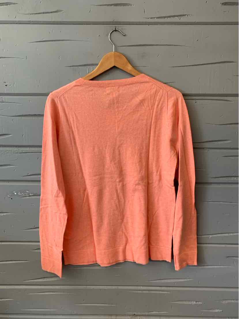 Coral long-sleeve lightweight knit sweater with crew neckline, displayed on wooden hanger against gray wood panel backdrop.