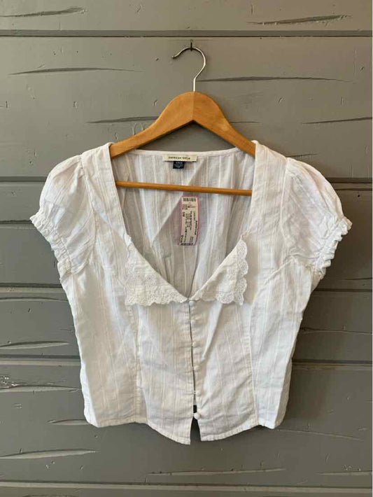 White short-sleeve blouse with deep V-neck and button-down front on wooden hanger.