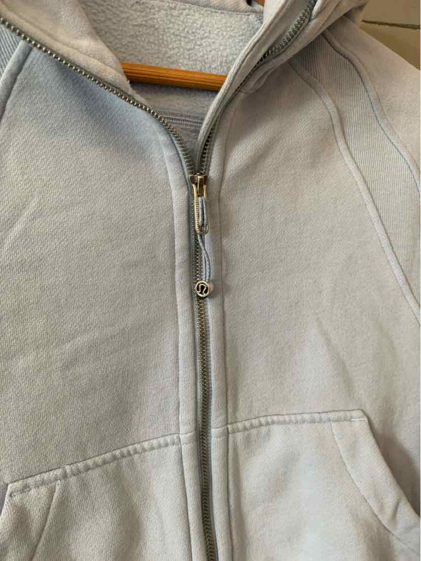 Light gray zip-up hoodie with silver zipper and front pockets, soft fabric, fitted seams.