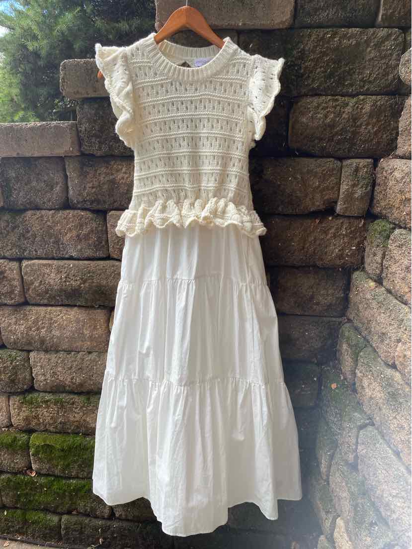 Cream crochet sleeveless top with ruffled hem paired with a tiered white maxi skirt on wooden hanger.