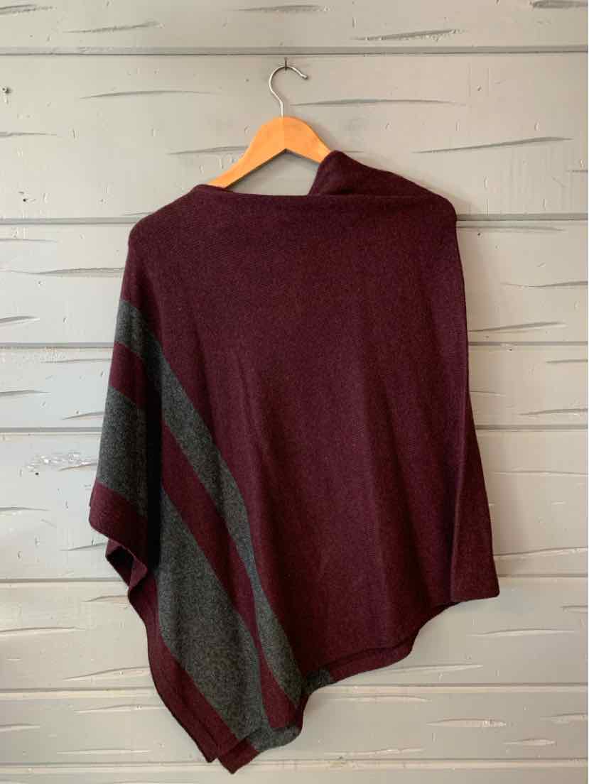 Burgundy knit poncho with dark gray diagonal stripes and a soft, draped fit hanging on wooden hanger.