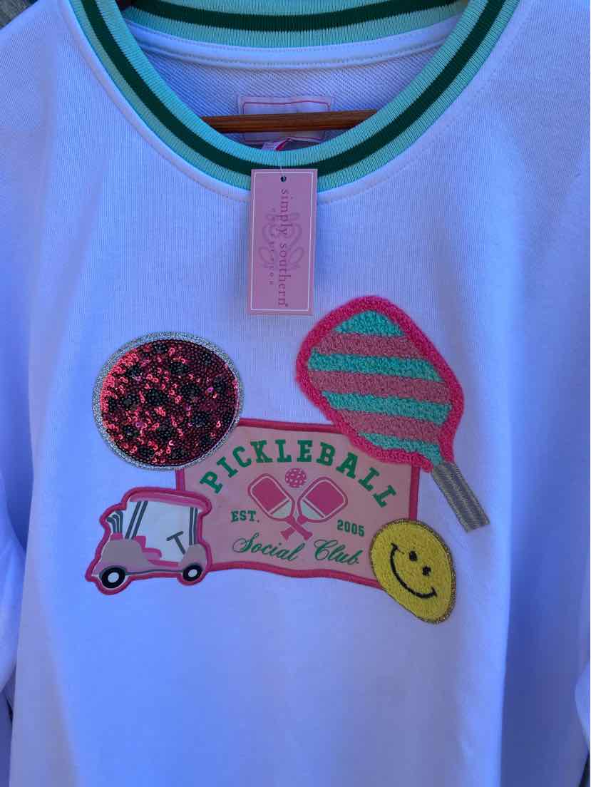 White long-sleeve shirt with teal and green striped collar, colorful pickleball-themed patches, and a smiley face patch on.