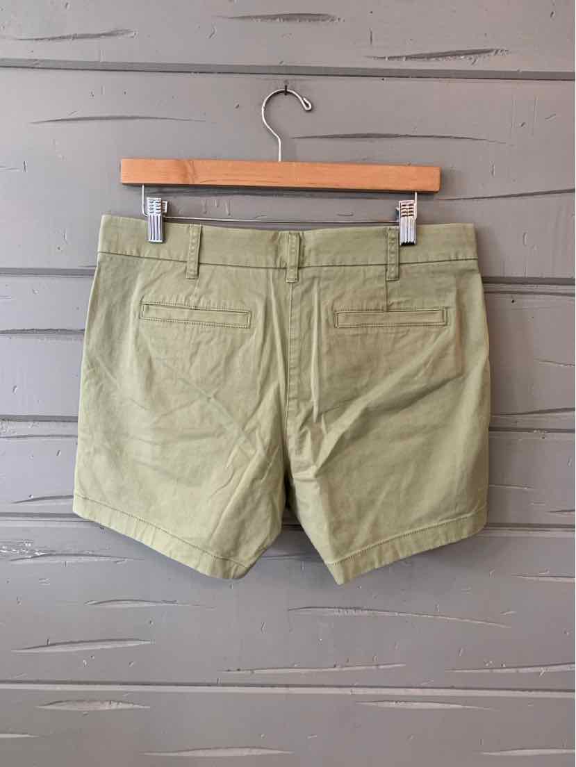 Light olive green cotton shorts with back welt pockets and belt loops hanging on wooden hanger.