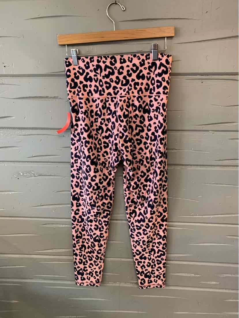 Pink leopard print leggings with high waist and slim fit hanging on wooden hanger against gray wooden wall.