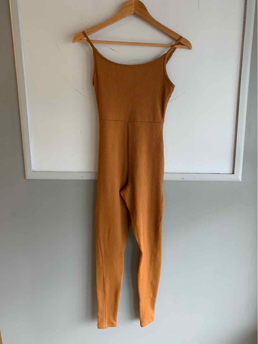 Copper-colored ribbed knit jumpsuit with spaghetti straps and fitted silhouette hanging on wooden hanger.